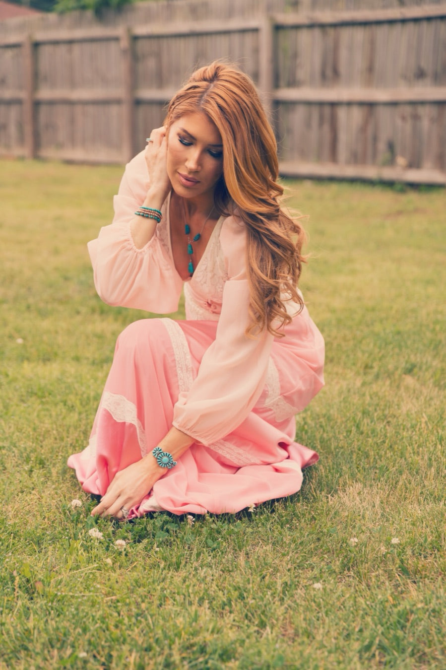 Kimberly Dawn kneeling in the grass in a pink prairie dress